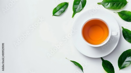 White cup of tea on white background with green tea leaves scattered around photo