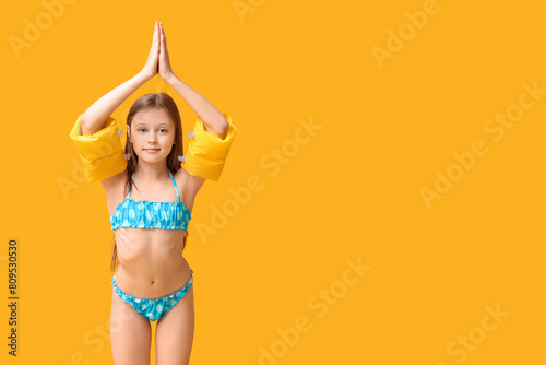 Cute little girl in swimsuit with inflatable armbands on yellow background photo