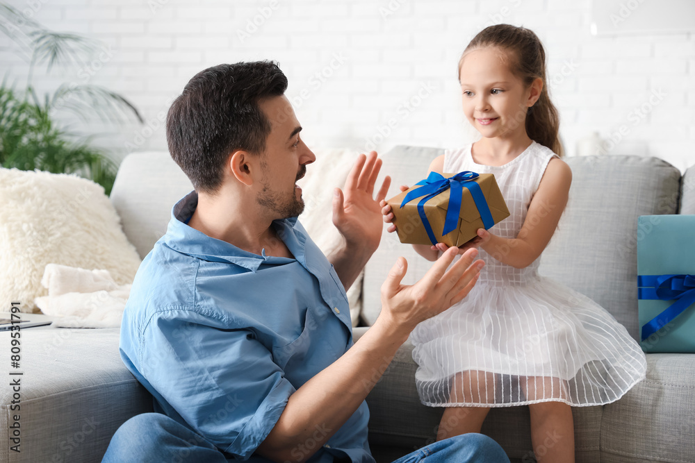Little daughter giving father present in living room. Father's Day celebration Little daughter giving father present in living room. Father's Day celebration