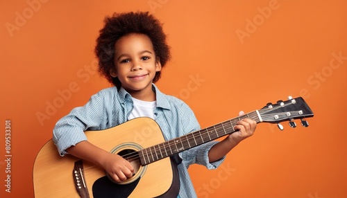 Joyful child playing guitar isolated on flat orange background