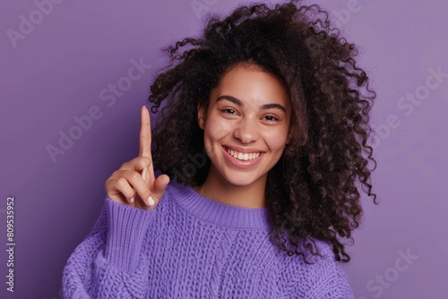 Happy smiling woman with curly hair wearing purple sweater pointing at something with finger photo