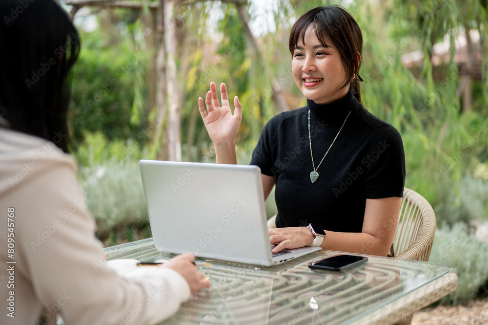 A cheerful Asian woman talking with her friend while working remotely in the garden. A cheerful Asian woman talking with her friend while working remotely in the garden.
