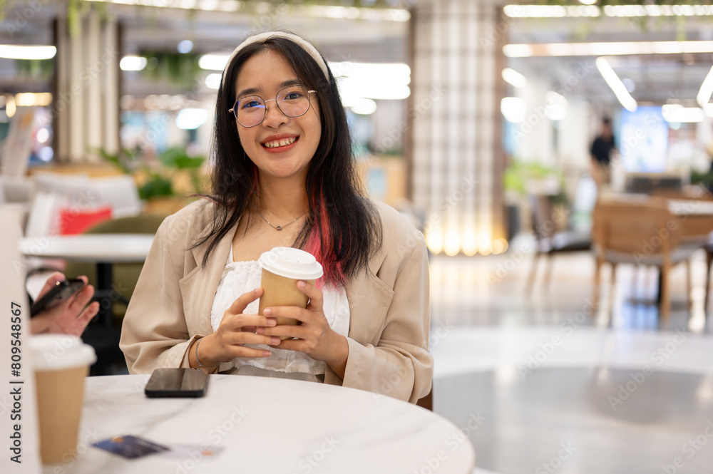 A beautiful young Asian woman in casual wear is sitting in a coffee shop in the shopping mall. A beautiful young Asian woman in casual wear is sitting in a coffee shop in the shopping mall.