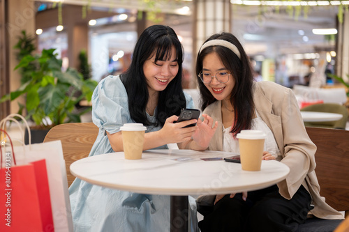 Two Asian female friends are relaxing in a cafe in the shopping mall after shopping together.