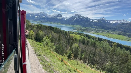 Tourist filming out of railway. View on lake sankt wolfgangsee from austrian alp mountain schafsberg. Red cog cable railway or touristic train in summer in Austria. Tourism of Salzkammergut.  photo