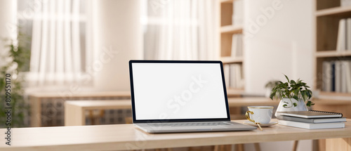 A white-screen laptop computer on a wooden table in a beautiful minimalist library or bookstore.
