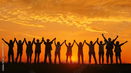 A group of people are holding hands in a field at sunset. Scene is one of unity and togetherness