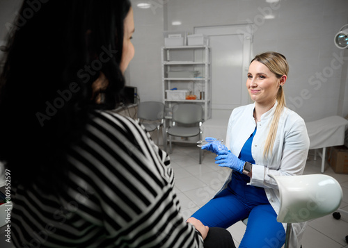 Pretty female doctor gynecologist in blue medical sterile gloves holding vaginal speculum. Obstetrical examination. Baby and mother healthcare check up. Women s health.