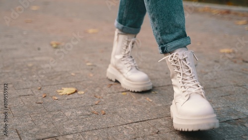 Young woman wearing jeans and stylish white boots while walking in the park. Close up. Seasonal style  autumn season concept. 