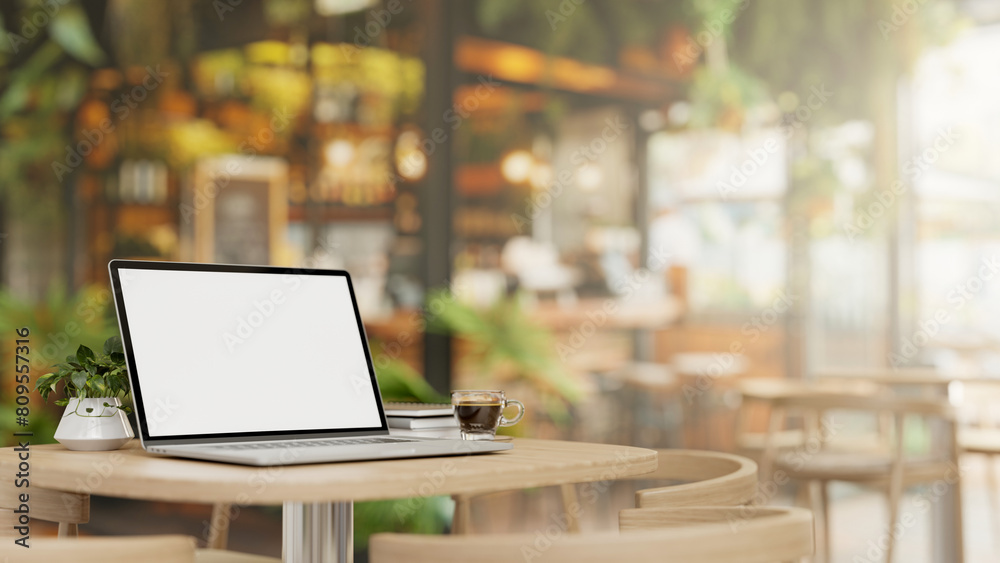 A laptop computer mockup and a coffee cup on a wooden table in a beautiful contemporary coffee shop.