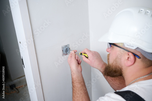 Crop view of electrician installing electric socket using screwdriver at construction site. Power socket installation. Installing a power outlet in to a plastic box on a wall.