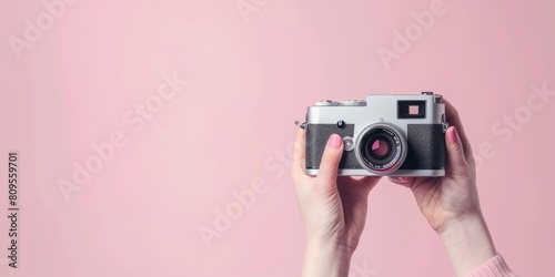 A person is holding a camera with a pink background. The camera is silver and has a black and white design