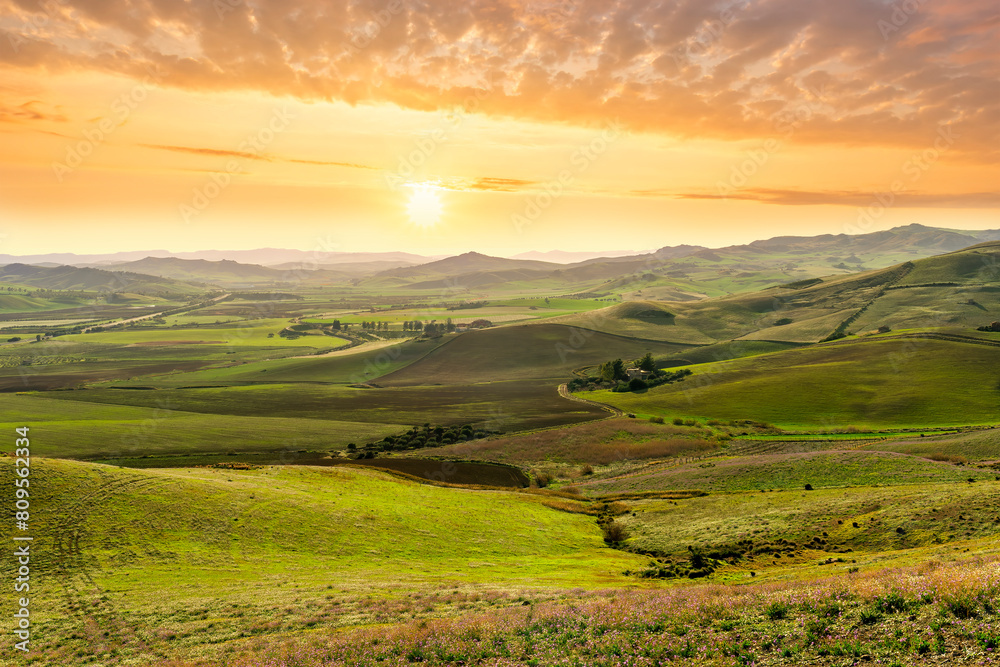 spring season green landscape of green field and meadow in a hill countryside with mountains and beautiful sunset sky on background