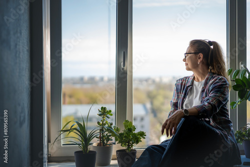 Caucasian attractive middle aged woman looking out the window at the city while from apartment © olezzo