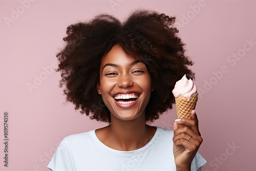 African young woman with a lush hairstyle eats ice cream in a waffle cone and smiles happily on a pink background