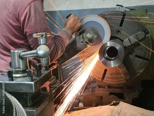 An engineering worker cutting stainles Steel bar with hand cutting grinder . mounted on lathe machine. photo