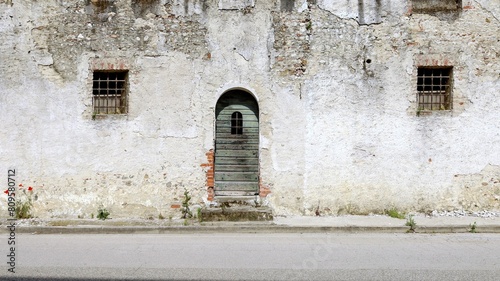 Old abandoned house with barred windows and arched door at the roadside. Background for copy space.