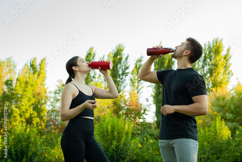 Pareja bebiendo agua en un parque. Mujer y hombre deportistas. Deporte al aire libre. Estilo de vida. Beber agua