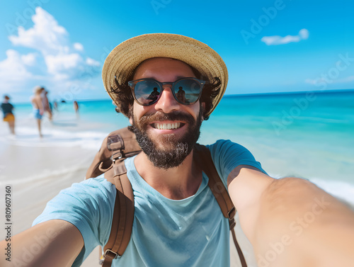 Young man with backpack smiling at camera on the beach and enjoying the freedom of taking a selfie on a sunny day. Wellbeing, healthy lifestyle and happy people concept
