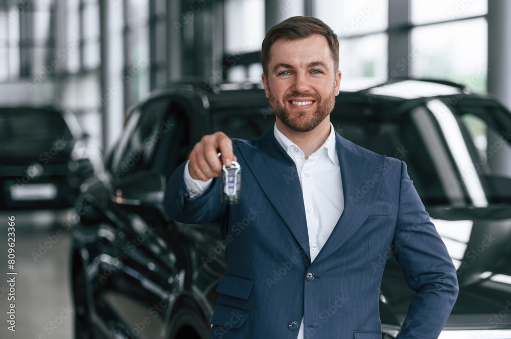 Keys in hand, smiling. A businessman is in a car dealership Keys in hand, smiling. A businessman is in a car dealership