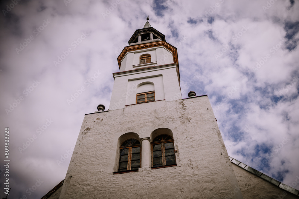 Valmiera, Latvia - August 25, 2023 - the tower of a white church set against a backdrop of dramatic cloudy skies, viewed from a low angle.
