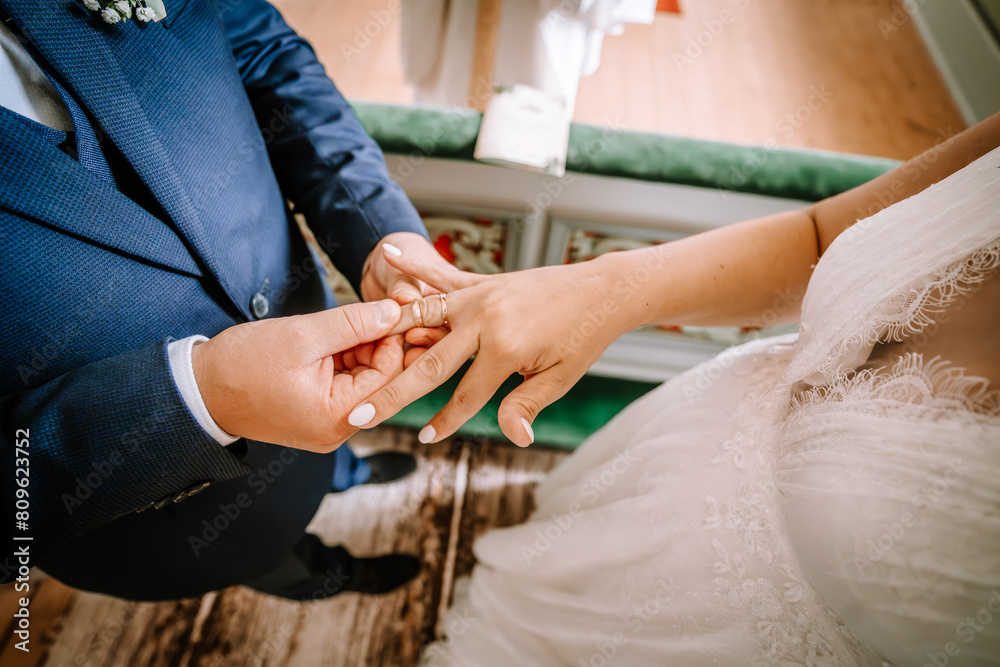 Fototapeta premium Valmiera, Latvia - August 25, 2023 - Close-up of a bride and groom exchanging wedding rings, focusing on their hands against a background of the bride's lace dress...