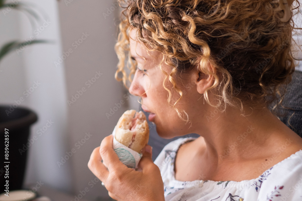One unhealthy woman eating sandwich and working on laptop at home ...