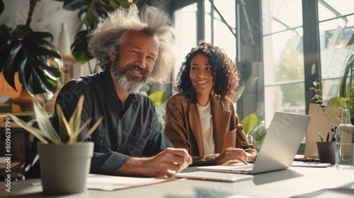 Two professionals in a modern office setting, a middle-aged Caucasian man with wild gray hair and a young African American woman with curly hair, smiling while discussing work at a bright, workspace photo
