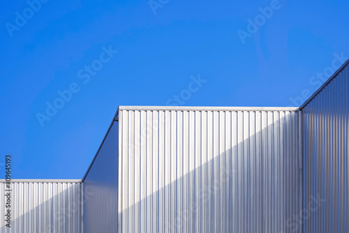 Aluminium corrugated steel wall of geometric industrial building against blue clear sky background in modern and minimal style, low angle and perspective side view