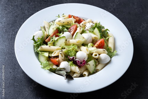 Pasta salad with vegetables and mozzarella cheese on black background. Close up