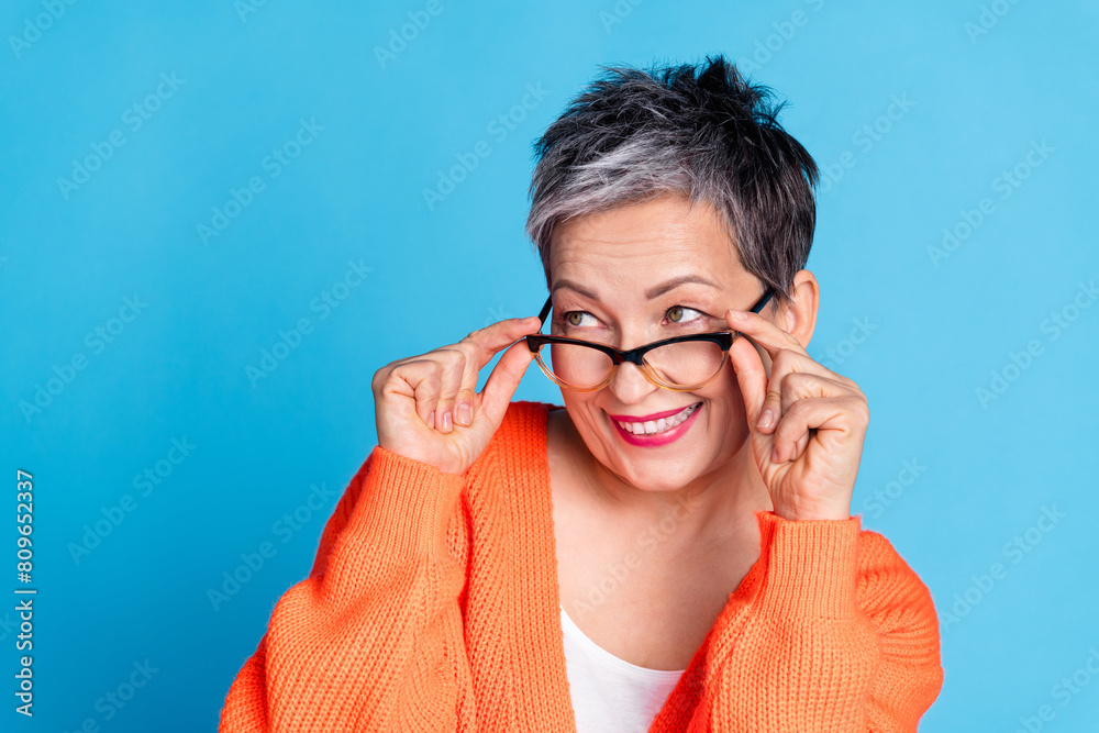 Photo portrait of lovely senior lady touch specs look empty space dressed stylish orange garment isolated on blue color background