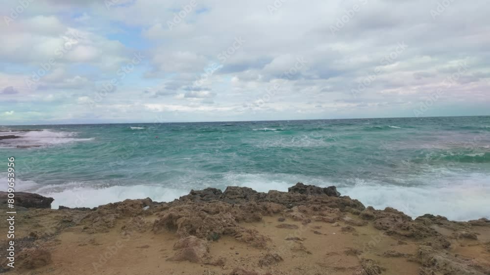 Waves gently roll onto a rocky beach under a partly cloudy sky, capturing the serene movement of the sea in slow motion Waves gently roll onto a rocky beach under a partly cloudy sky, capturing the serene movement of the sea in slow motion
