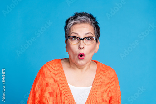 Photo of aged lady pouted lips stare wear orange cardigan isolated on blue color background photo