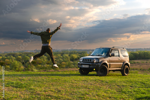 a happy man is jumping towards adventure on his off-road vehicle. Hands spread to the sides. The concept of active lifestyle and vacation road trip. A travelling by car to wilderness.