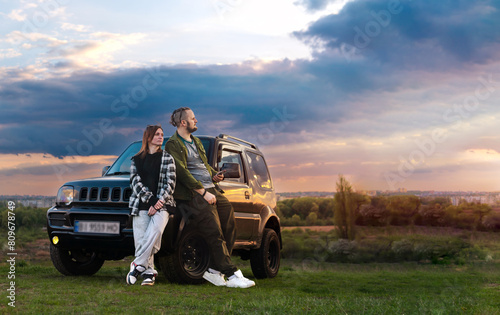 Travelers Couple. Road Trip, Man and Woman on Journey Near Their SUV off road Car Over Beautiful Landscape. Sunset clouds. Copy space.