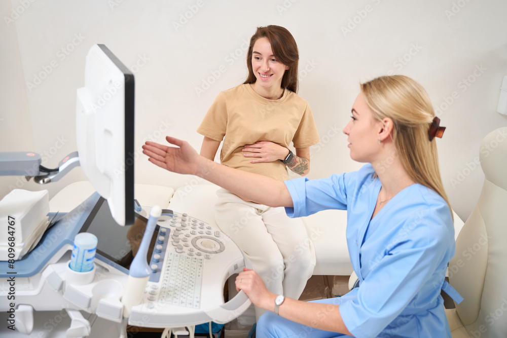 Obraz premium Gynecologist showing result of ultrasound scanning to pregnant smiling woman