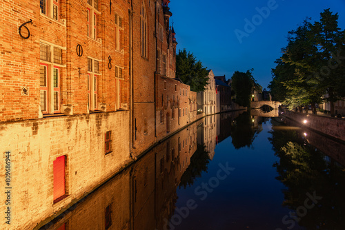 Historic buildings reflected on the canal in the old town of the beautiful city of Bruges in Belgium with the Meestrat bridge in the background at night. photo