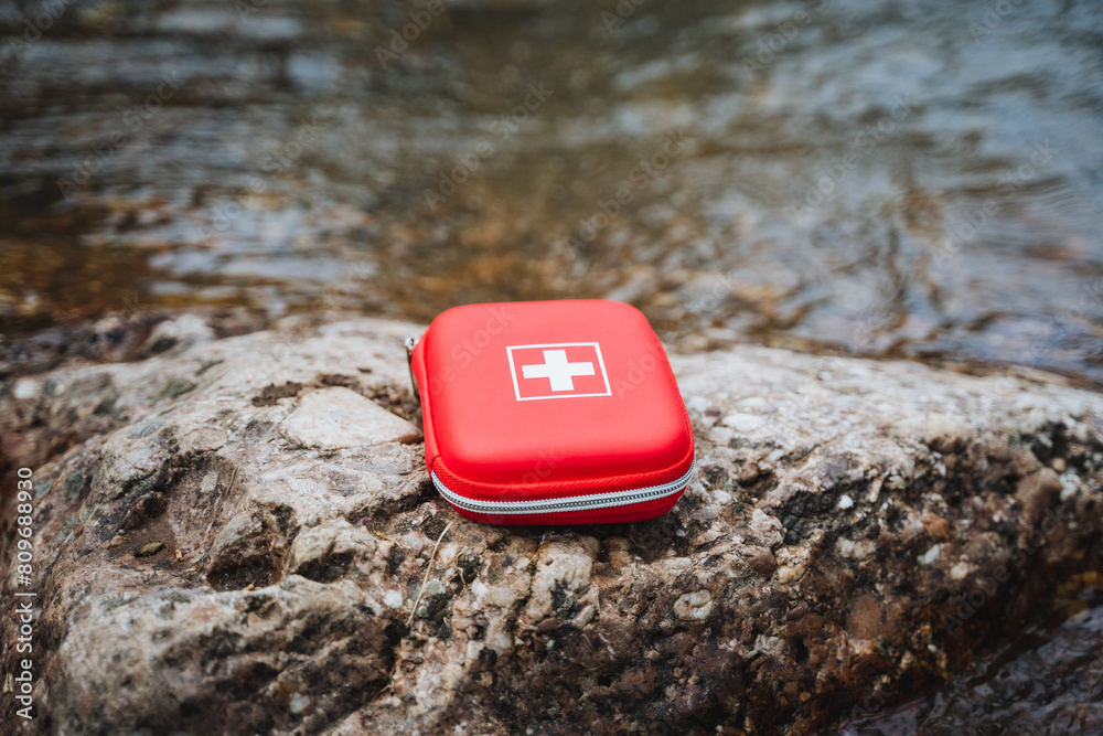 Naklejka premium A red first aid kit rests on a rock beside the river