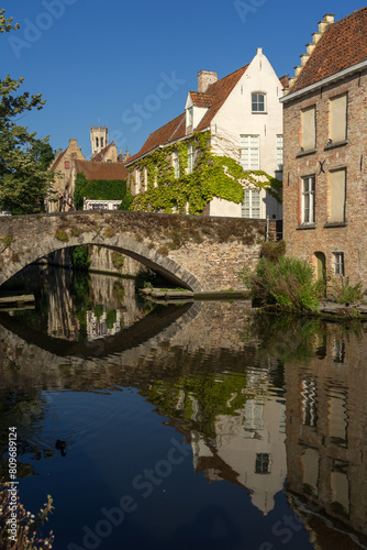 Peerden bridge and historic buildings reflected on the canal in the old town of the beautiful city of Bruges in Belgium in a sunny day. © JoseLuis