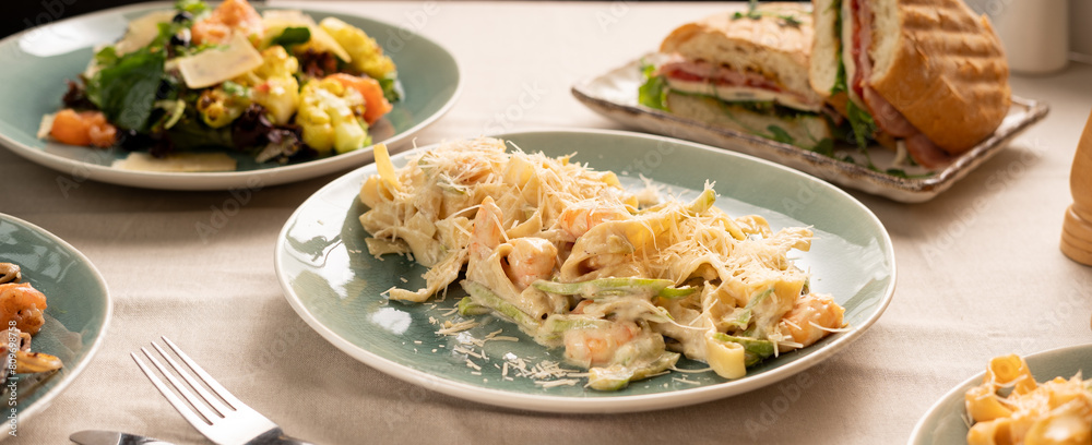 Fettuccine pasta with shrimp in a creamy sauce with cheese served on a plate on the table with other dishes for dinner Fettuccine pasta with shrimp in a creamy sauce with cheese served on a plate on the table with other dishes for dinner