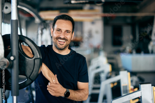 A smiling fitness man posing for the camera while standing next to a barbell with weights on.
