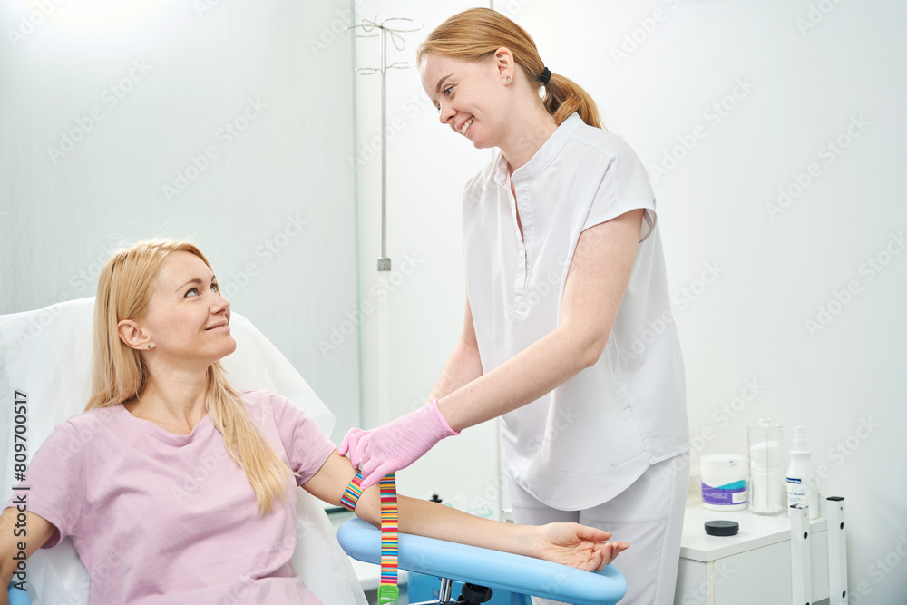Female client smiling to friendly nurse who preparing her for blood donation Female client smiling to friendly nurse who preparing her for blood donation