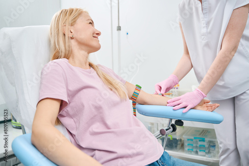 Female patient sitting in medical couch while nurse putting intravenous in