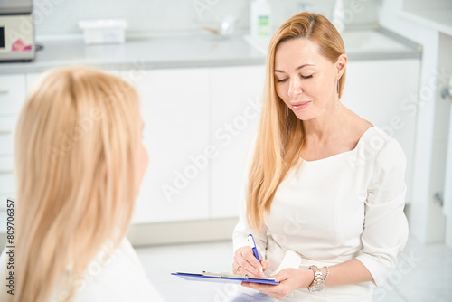 Attractive doctor filling in medical records talking with patient