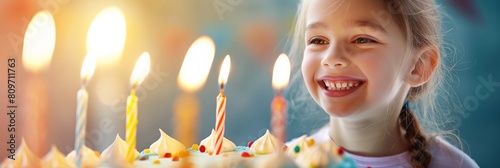 Close-up of a cheerful little girl smiling widely at lit birthday candles on a beautiful cake photo
