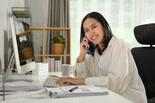 Beautiful businesswoman sitting at working desk and talking on mobile phone © Prathankarnpap