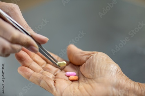 A hand holding a pair of tweezers is picking up a pill from an open palm.