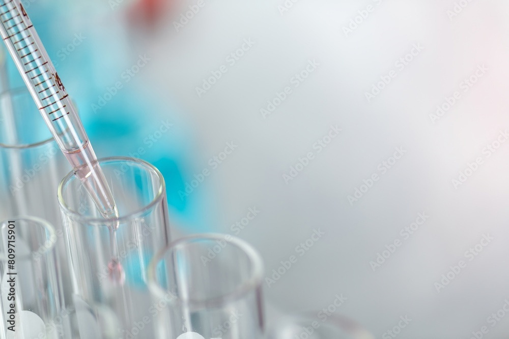 A close up of a pipette adding a red liquid to a test tube in a laboratory with a blurred background A close up of a pipette adding a red liquid to a test tube in a laboratory with a blurred background