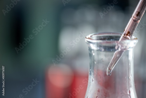 Close-up of a graduated conical flask with a red liquid being added from a dropper.