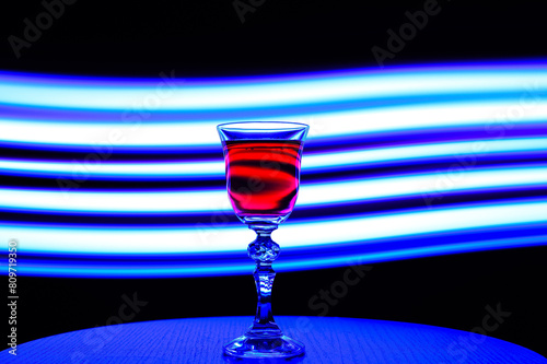 Efektowny kryształowy kieliszek na wino postawiony na tle smug światła w niebieskim kolorze 